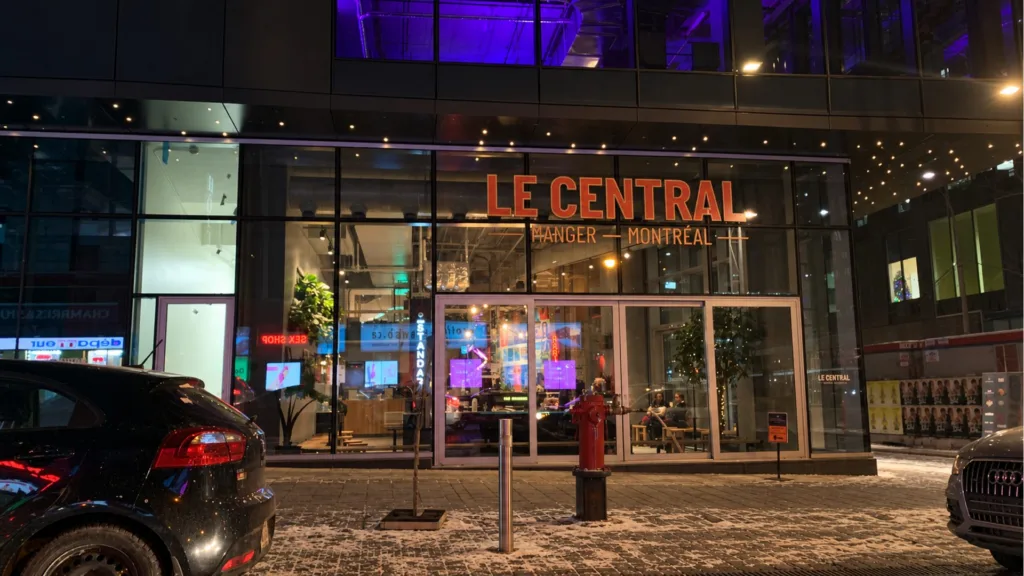 Façade vitrée de Le Central la nuit, avec son enseigne lumineuse