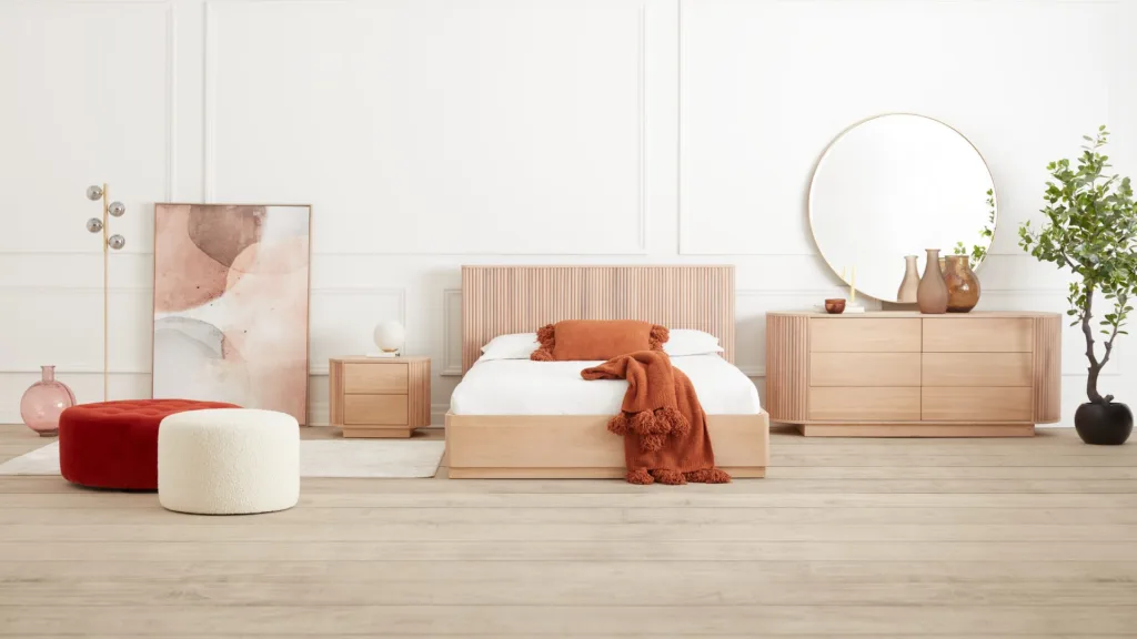 Chambre avec lit en bois clair, couvre-lit orange et poufs rouges