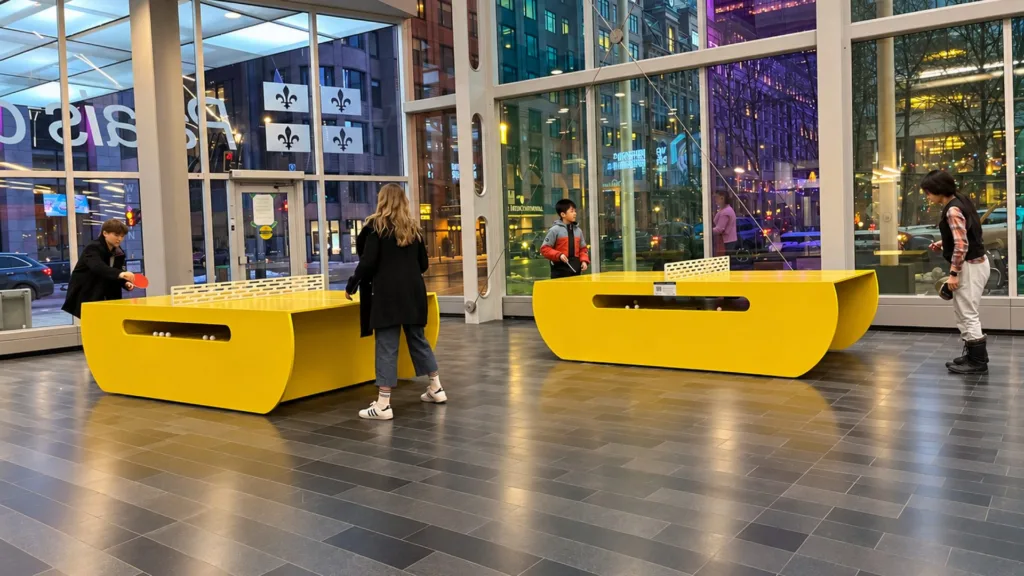 Grandes tables jaunes dans le hall vitré, avec des passants